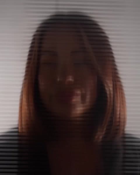 A woman with long copper hair seen through window blinds
